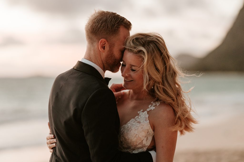 A bride and groom embrace by the ocean at sunset