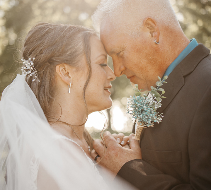 A bride touches foreheads with a smiling older man on her wedding day
