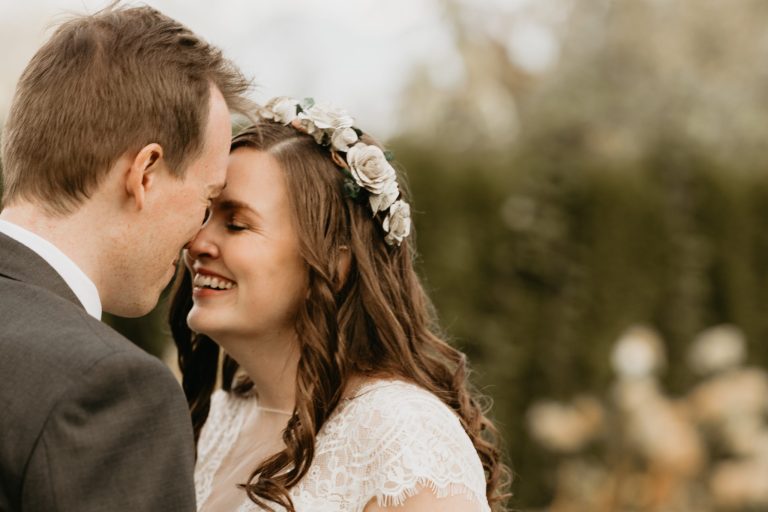 A bride in a flower crown and her groom share a quiet laugh, foreheads close