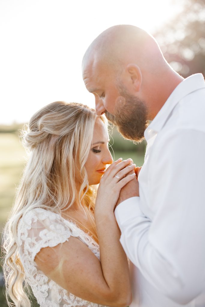 A groom kisses his bride's forehead as she smiles with her eyes closed