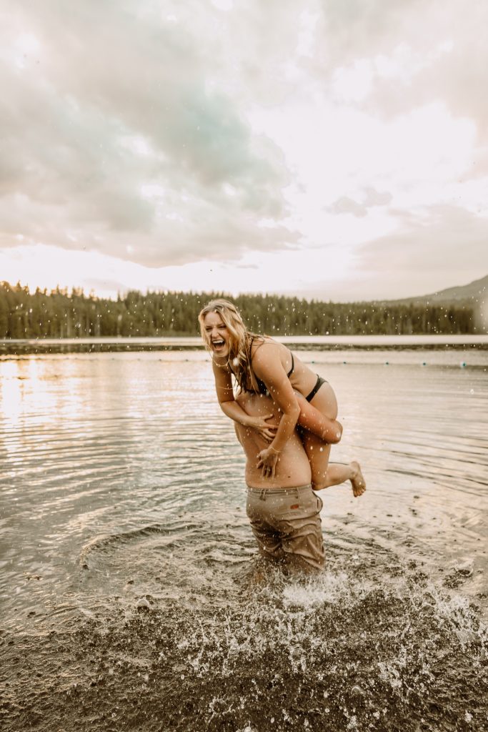 Playful couple takes a spontaneous dip in the lake, candid engagement shoot