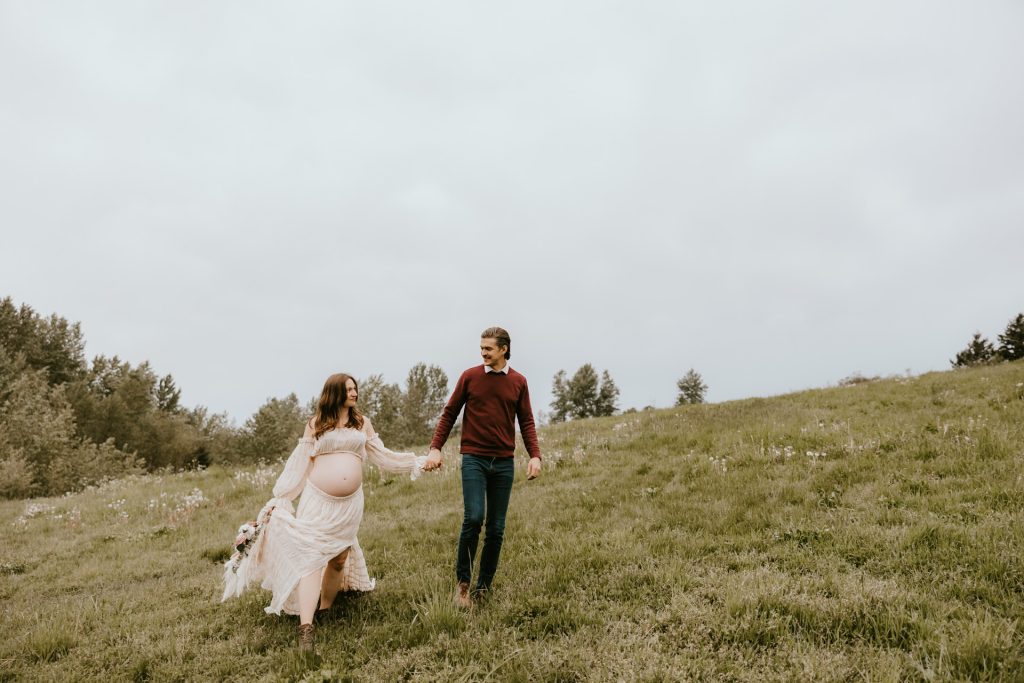 Pregnant woman posing in a sunlit meadow in Fraser Valley, BC, with vibrant wildflowers in the background.