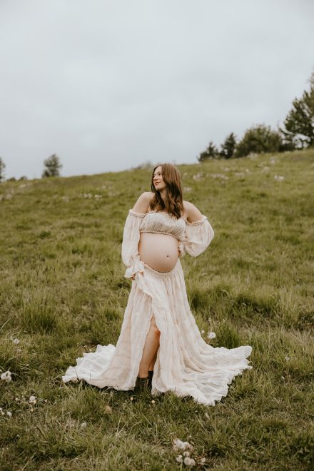 Expectant mother in a flowing dress standing in a lush Fraser Valley meadow during a maternity photoshoot.