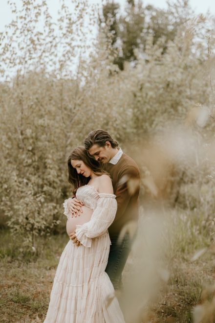 Mother-to-be cradling her baby bump in a serene meadow setting in Fraser Valley, surrounded by nature.