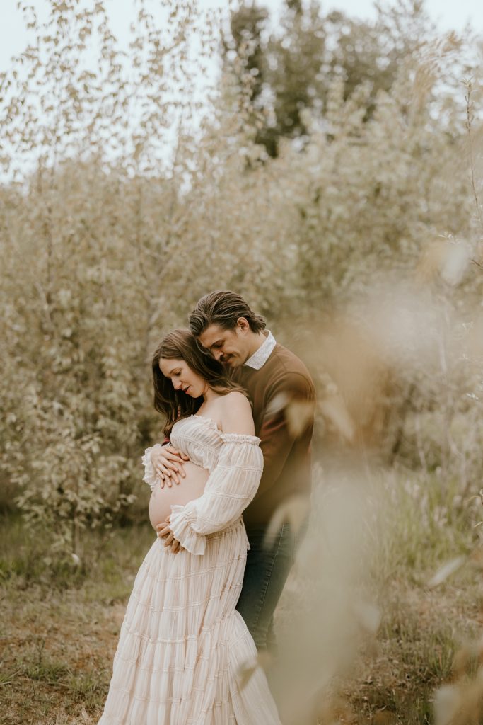 Mother-to-be cradling her baby bump in a serene meadow setting in Fraser Valley, surrounded by nature.