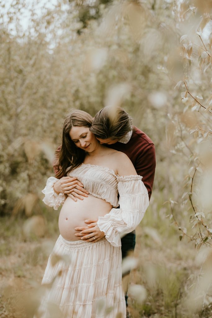 Pregnant woman posing in a sunlit meadow in Fraser Valley, BC, with vibrant wildflowers in the background.