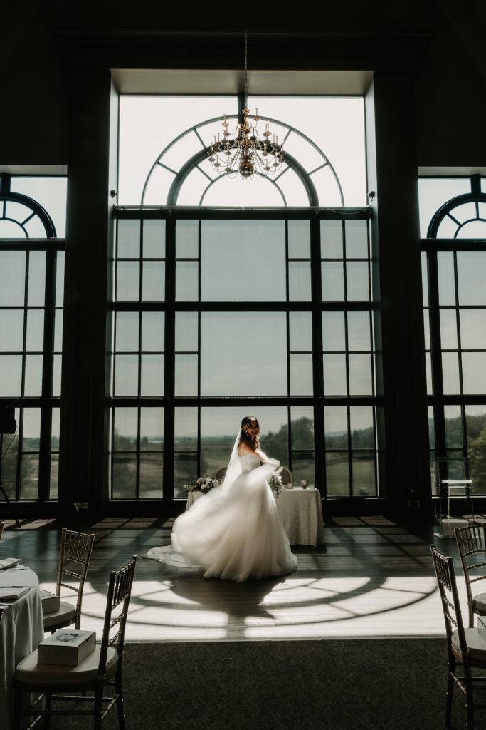 A bride twirls her dress beneath a tall arched window