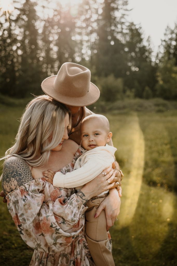 Parents holding their 10-month-old son together in tall field grasses