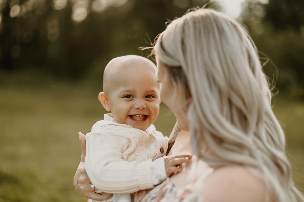 Close-up of baby smiling while nestled between mom outdoors