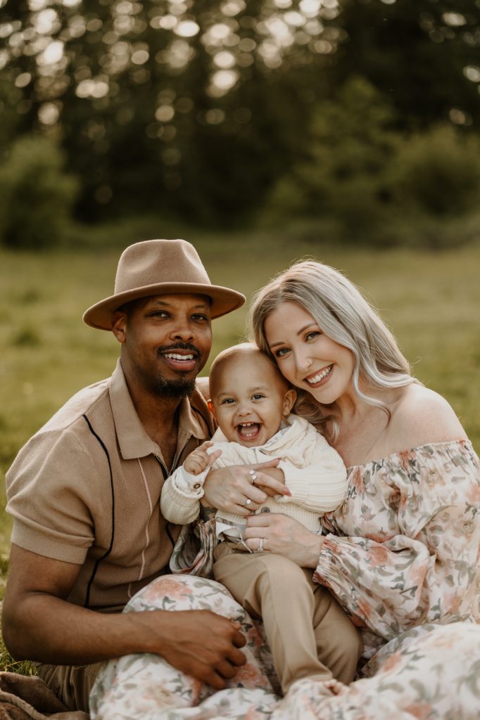 Parents in a sunny Maple Ridge meadow hold their laughing baby boy