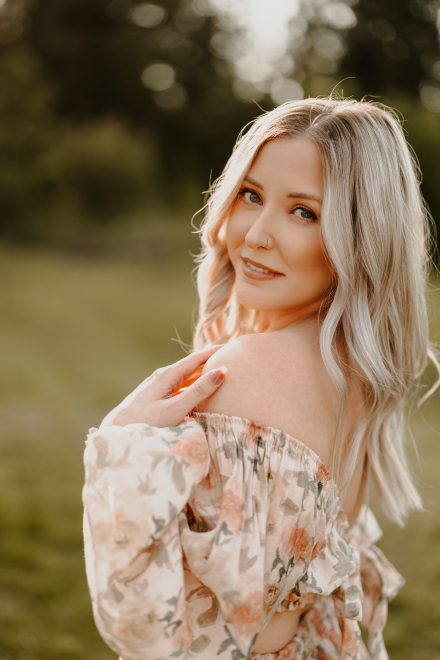 Portrait of woman standing alone in golden meadow, softly lit by evening sun