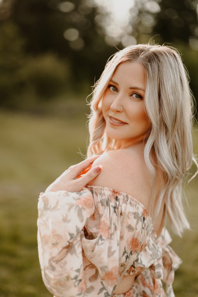 Portrait of woman standing alone in golden meadow, softly lit by evening sun