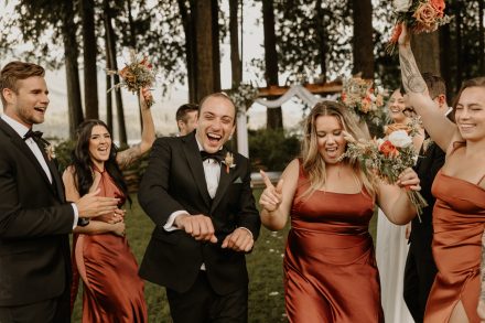 Fun bridal party dancing together across riverside lawn at Rowena’s venue