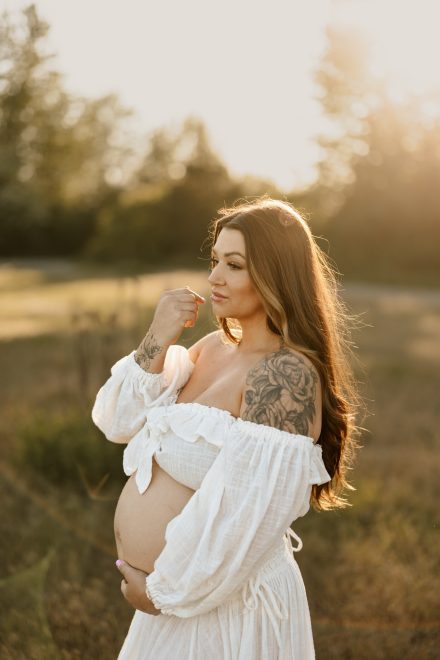 Sunset maternity session in grassy meadow at Blackie Spit featuring flowing dress and soft smiles