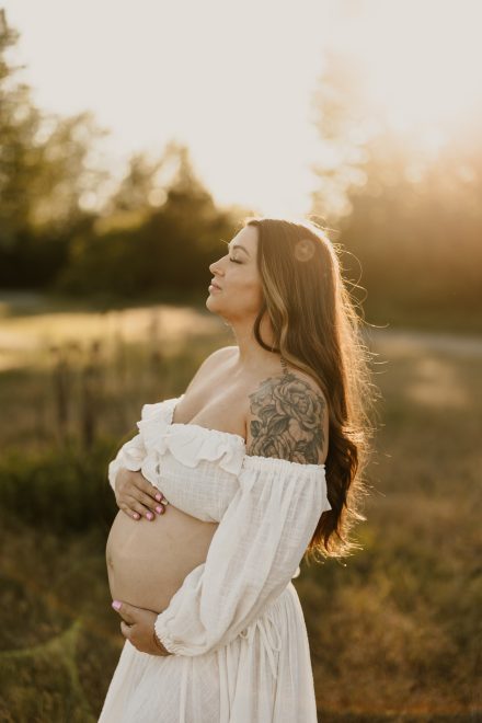 Tender maternity portrait with hands on belly in warm light at Blackie Spit natural setting
