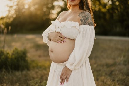 Peaceful moment of mama-to-be standing barefoot in meadow during golden hour shoot