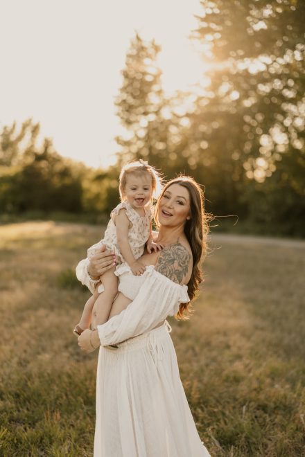 Timeless outdoor maternity portrait in soft dress surrounded by wildflowers and sunlight