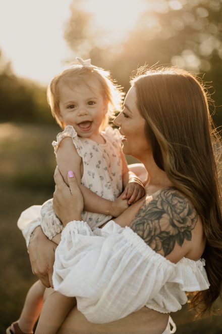 Glowing pregnancy photo in flowing gown with golden backlight in quiet meadow setting