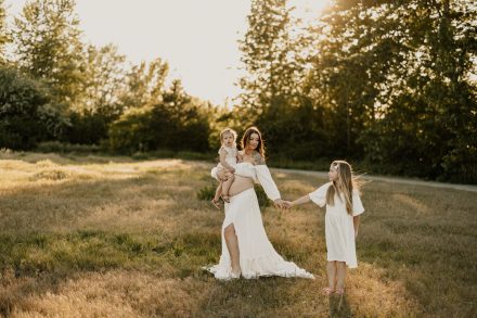Soft focus maternity shot of mama holding her belly in sun-drenched field at Blackie Spit