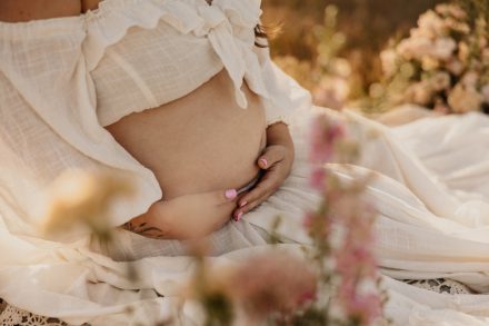 Glowing mother-to-be in flowing maternity dress standing in golden meadow at Blackie Spit Vancouver