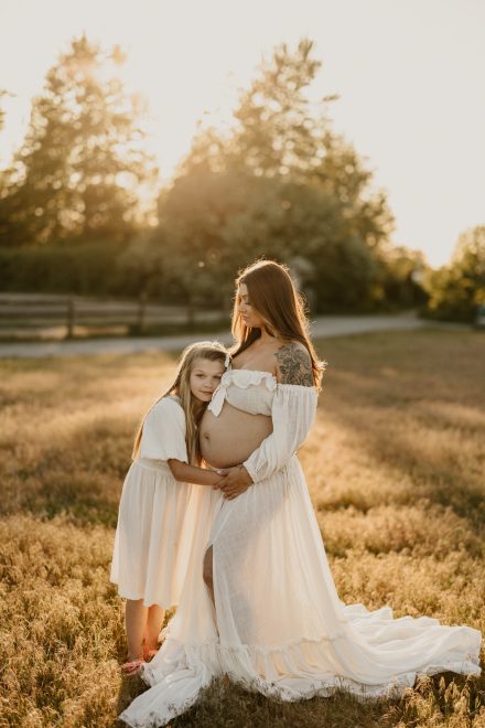 Dreamy maternity session in open grassy field with romantic dress and golden sunset tones