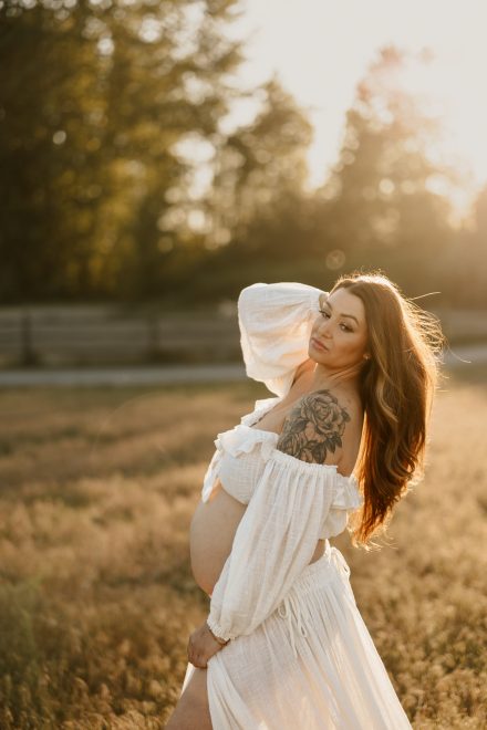 Timeless outdoor maternity portrait in soft dress surrounded by wildflowers and sunlight