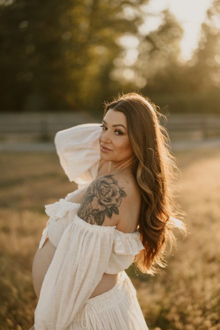 Glowing pregnancy photo in flowing gown with golden backlight in quiet meadow setting