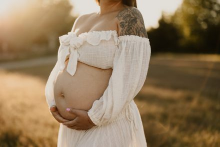 Sunset maternity session in grassy meadow at Blackie Spit featuring flowing dress and soft smiles