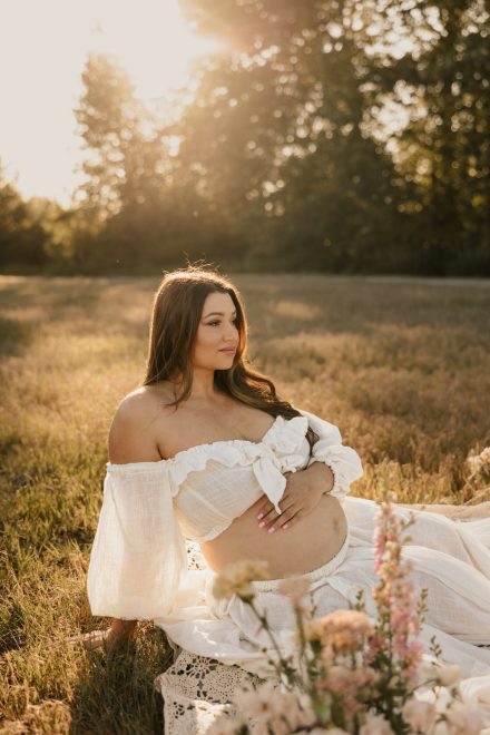 Golden hour maternity session with expecting mother cradling belly in serene grassy field