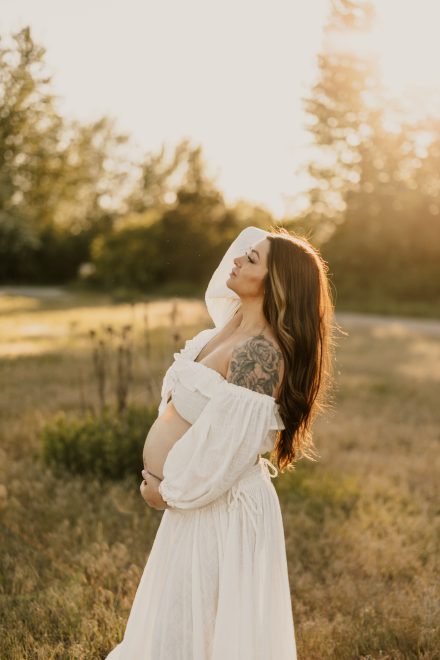 Golden maternity moment in peaceful meadow with flowing gown catching the light