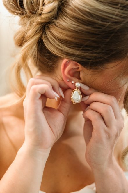 Bride sliding on her earrings in soft natural window light, photographed by Kate Paterson Photography