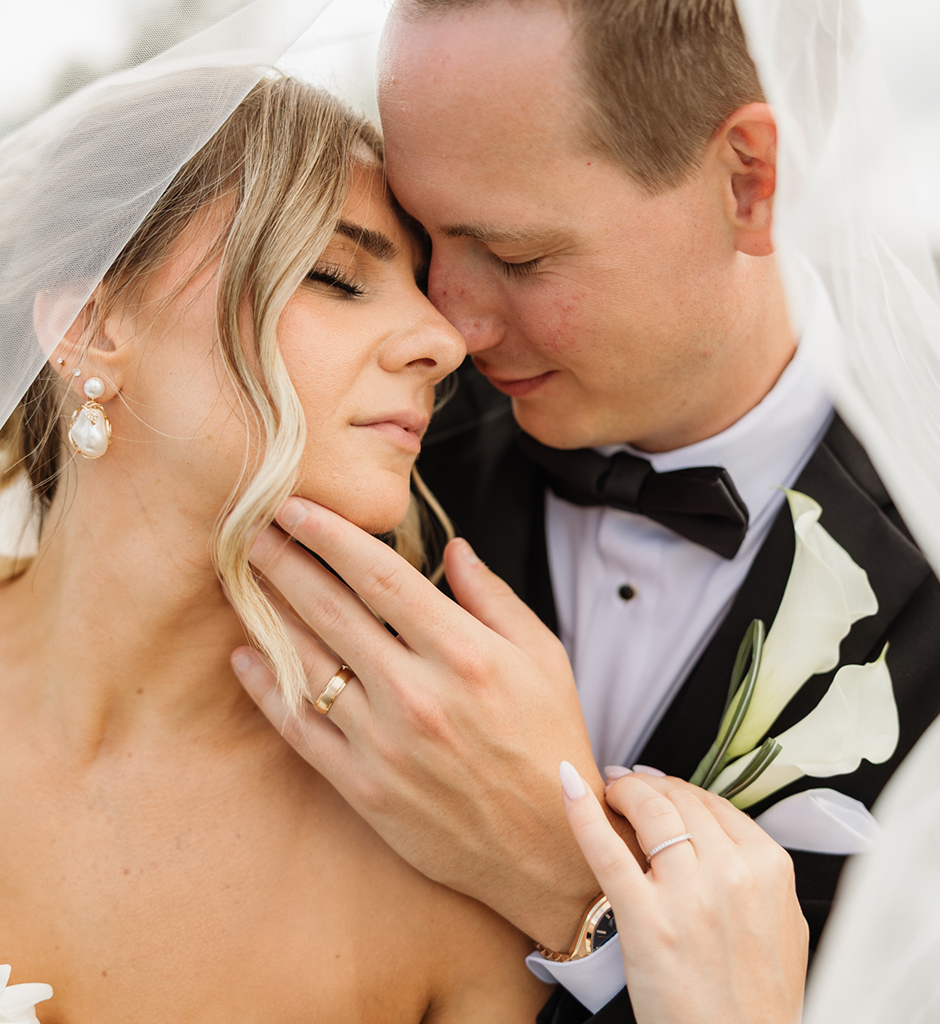 A groom kisses his bride's temple as she rests her hand on his chest, eyes closed