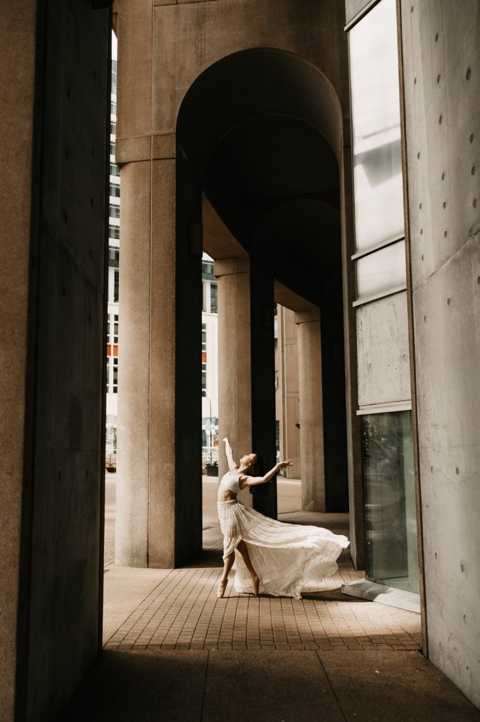 A dancer in a flowing gown poses between tall concrete arches