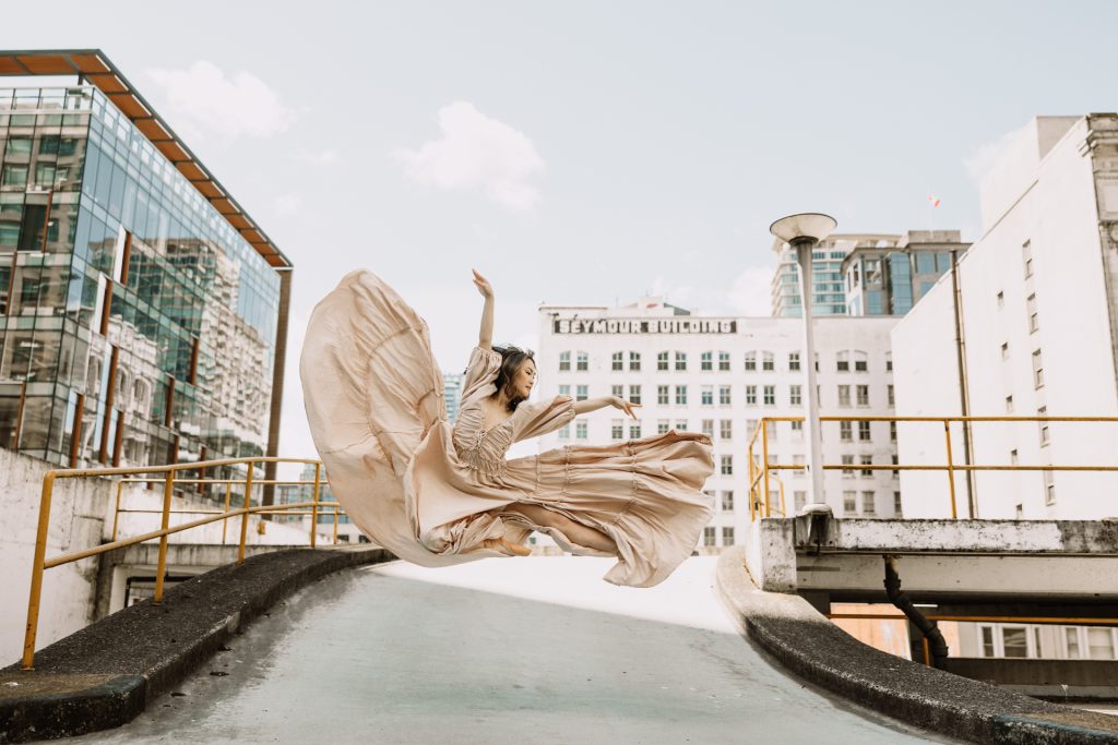 A dancer leaps on a city rooftop, her long gown flying behind her