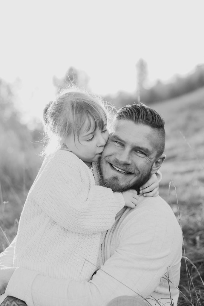 Black and white photo of a little girl hugging her dad, who grins at the camera