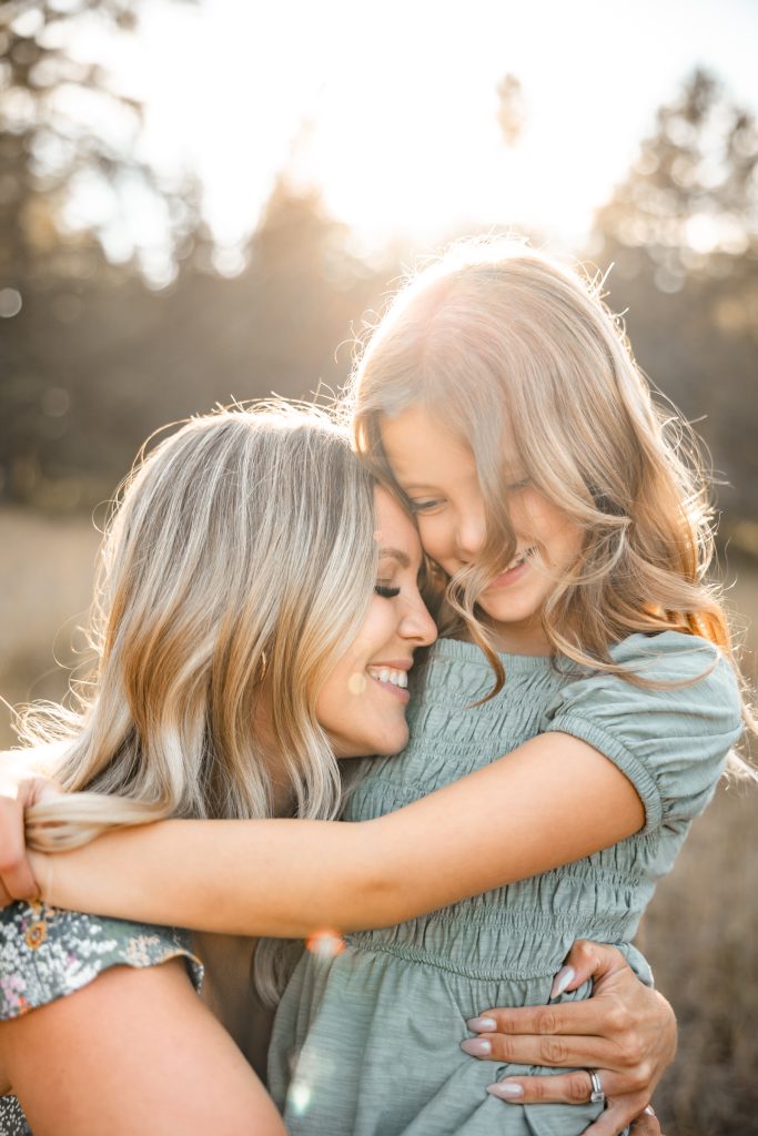 A mother and her daughter share a laughing hug in the backlit grass