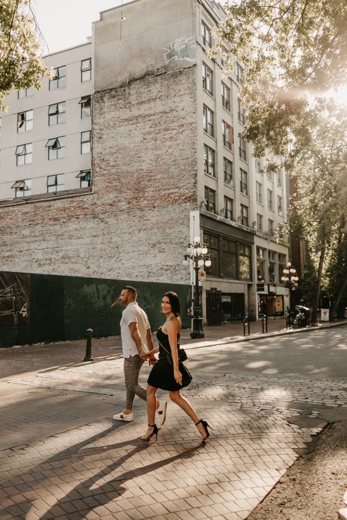 A couple stroll hand in hand down a sunlit Gastown street