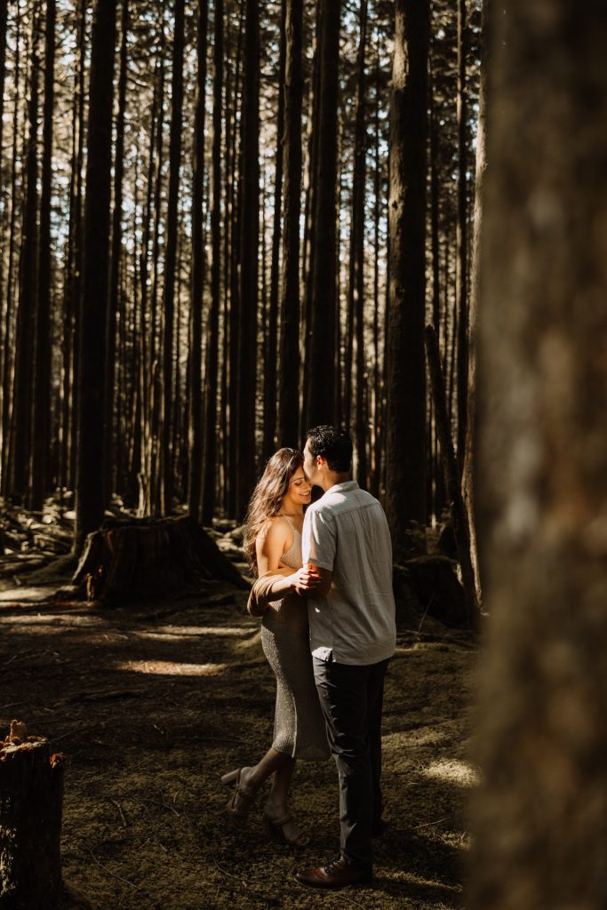A couple walk together through a sun-dappled forest of tall trees