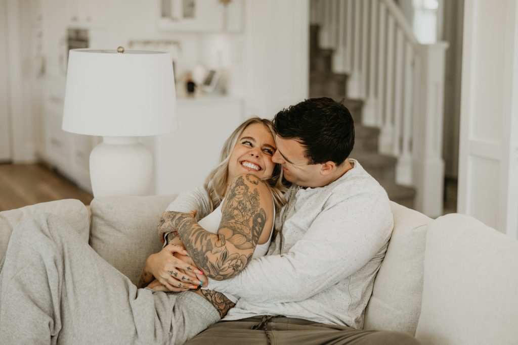 A couple cuddle and laugh on a white sofa at home