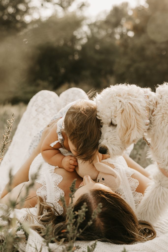 A baby in a white dress meets the family's fluffy white dog nose to nose in the grass