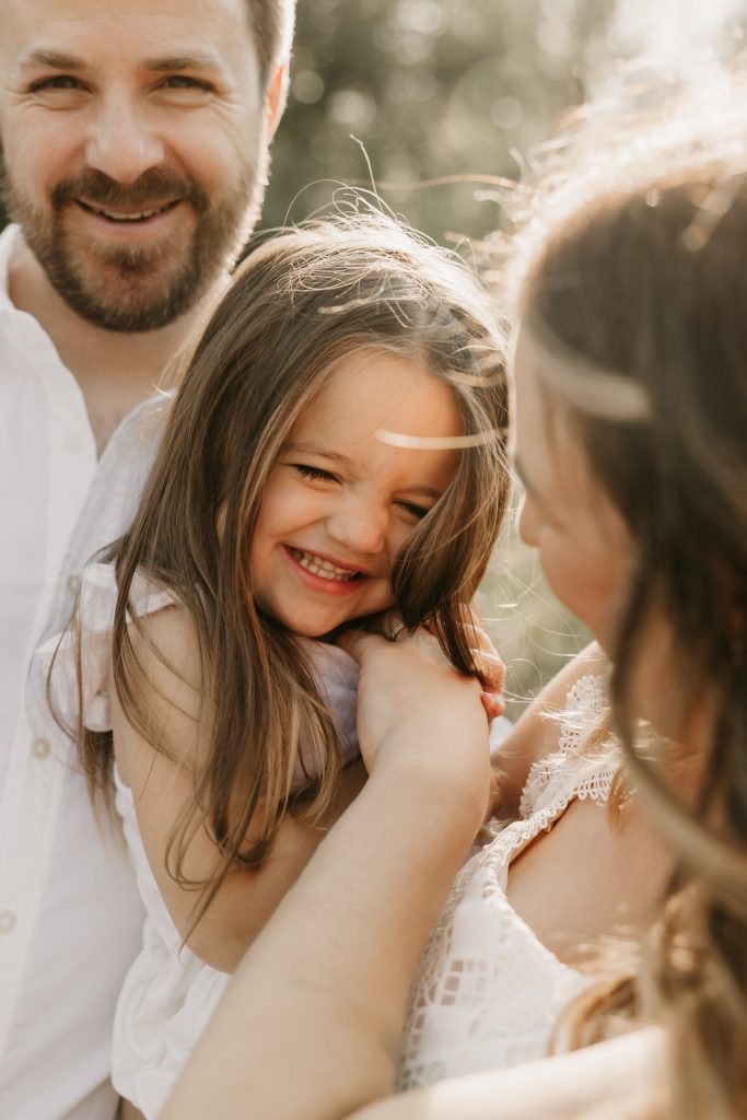 A little girl laughs as her parents hug her close