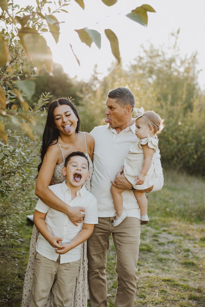 A family of four laughs together in a sunny meadow