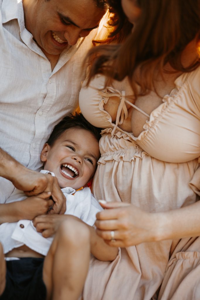 A mother in a blush dress laughs with her giggling toddler on her lap