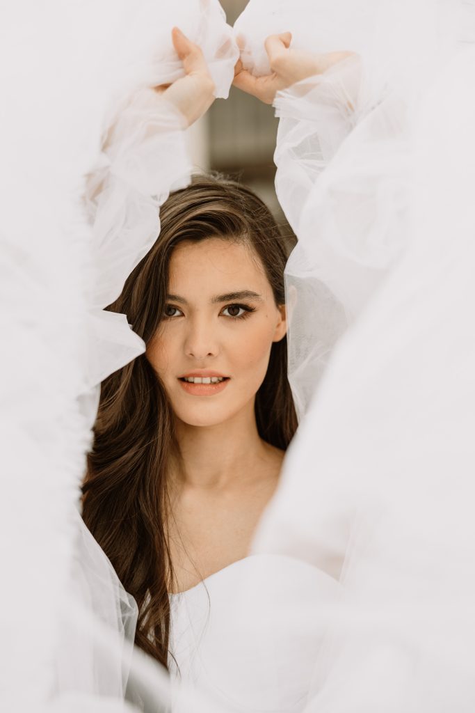 A woman with long dark hair gazes at the camera, framed by soft white tulle