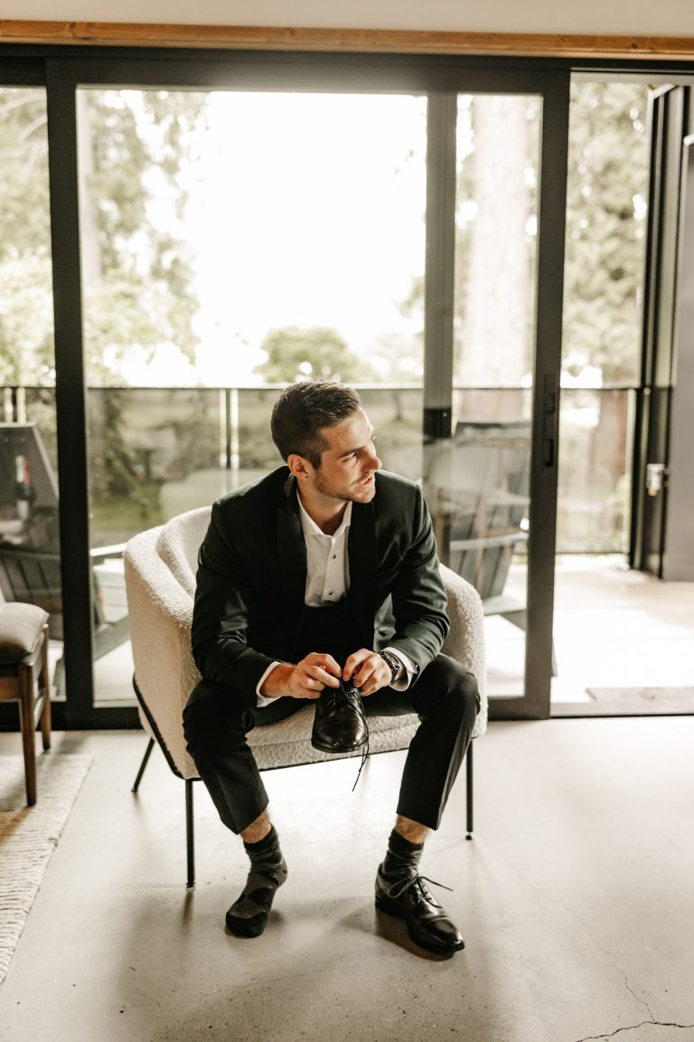 A groom sits quietly in a sunlit room on the morning of his wedding