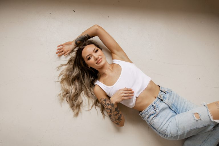 A woman in a white crop top and jeans lies laughing on a white studio floor