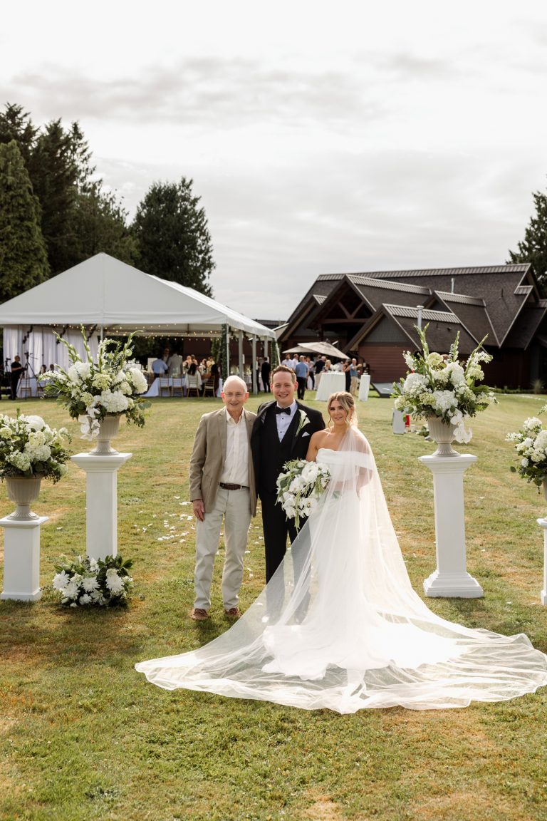 A bride is walked up a grass aisle lined with white flowers
