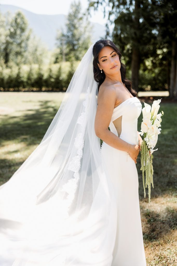 A bride holds her bouquet as her long veil drifts in the breeze