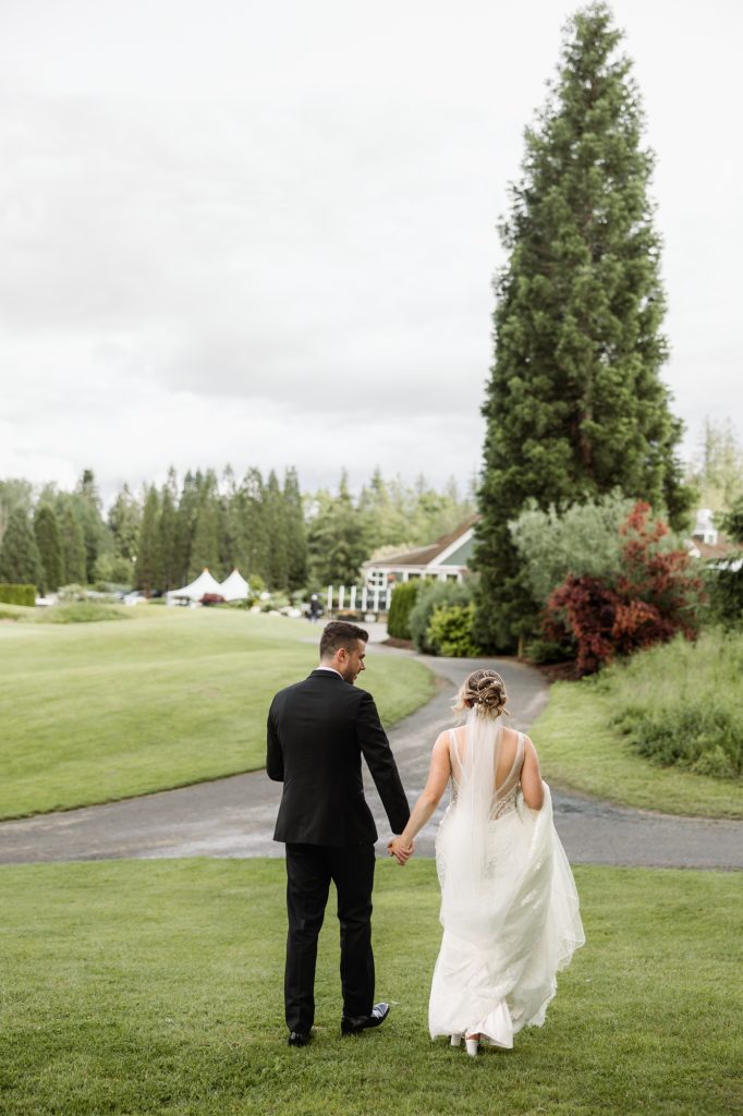 A bride and groom walk hand in hand across a golf course lawn