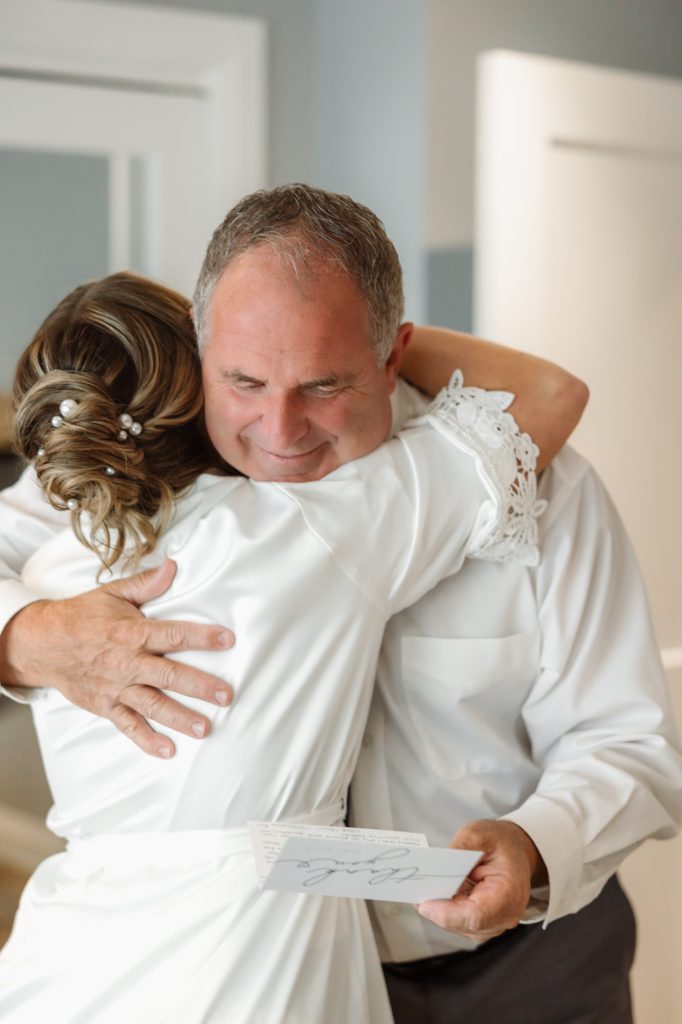 A bride shares an emotional hug with an older man holding a card